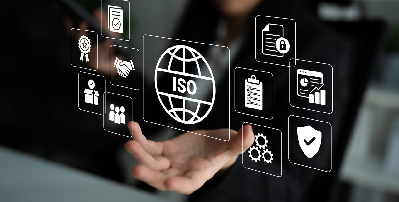 A businessman interacts with floating ISO standard icons in a modern corporate workspace, illustrating the importance of quality management and digital solutions for business success.