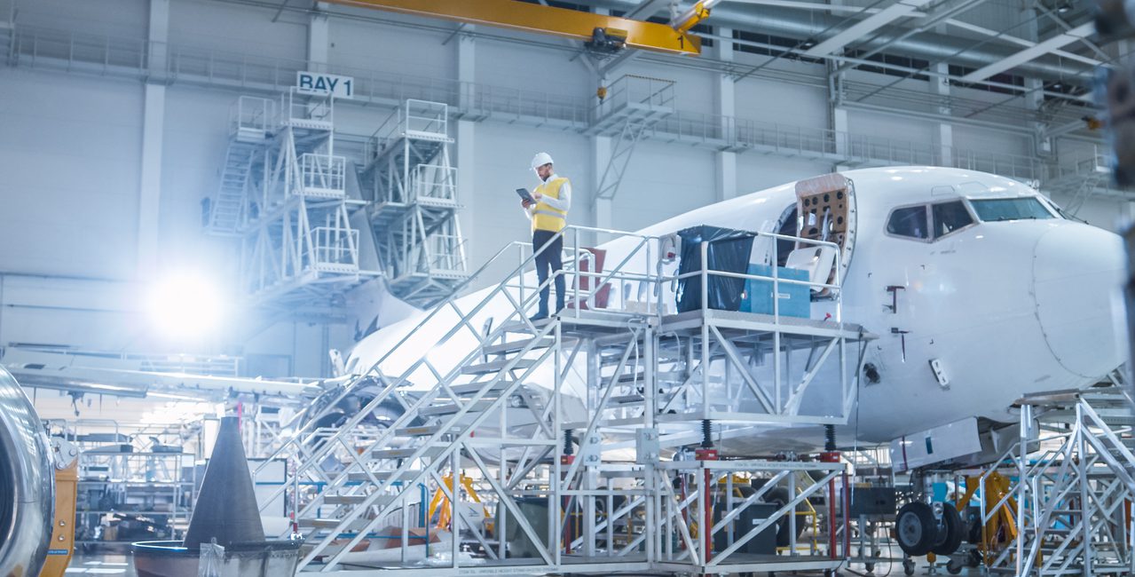 Engineer in Safety Vest Standing next to Airplane in Hangar