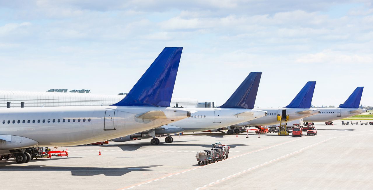 Tails of some airplanes at airport during boarding operations. They are four planes on a sunny day, with a blue sky. Travel and transportation concepts.