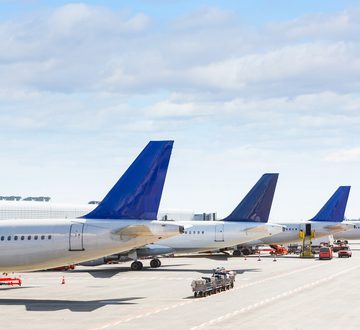 Tails of some airplanes at airport during boarding operations. They are four planes on a sunny day, with a blue sky. Travel and transportation concepts.