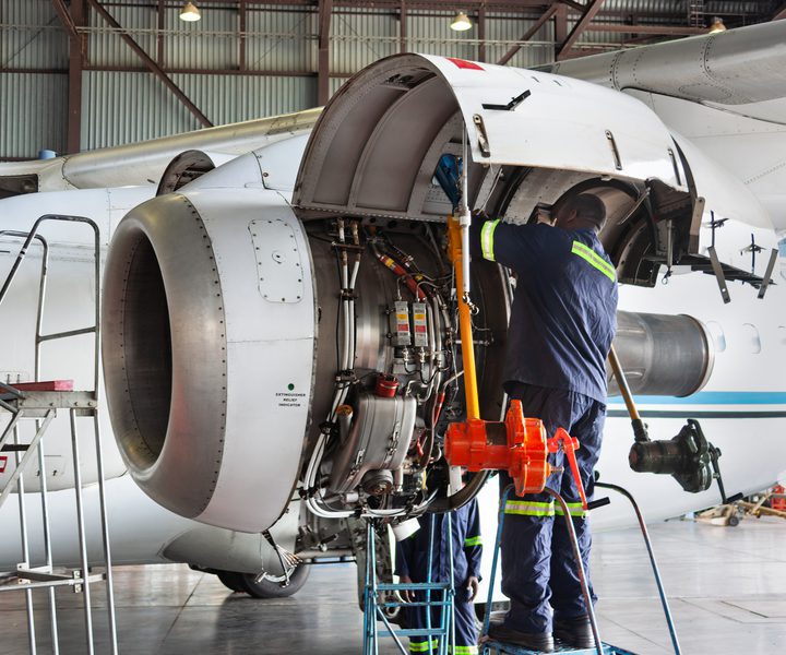 Two plane technicians working on open turboprop airplane engine during mechanical inspection and repair inside hangar.