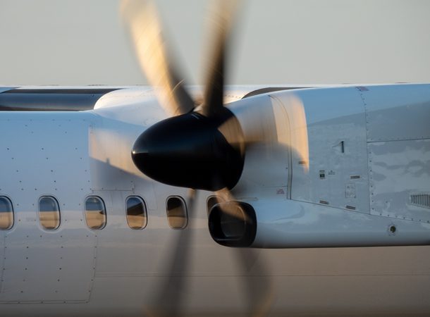A Qantas De Havilland Canada Dash 8-400 plane, registration VH-QOM, taxiing to the third runway of Sydney Kingsford Smith Airport as flight QF2008 to Tamworth. The setting sun reflects on the propellers. This image was taken from near General Holmes Drive, Mascot on a hot and sunny evening approaching sunset on 24 January 2025.